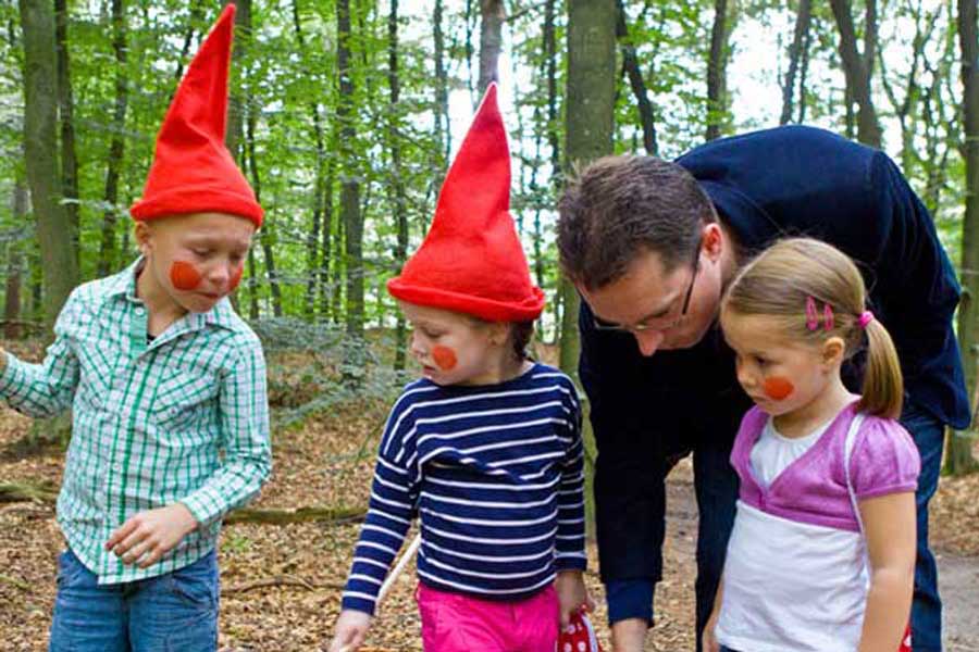 Drie kinderen lopen verkleed als kabouter met hun vader door het bos