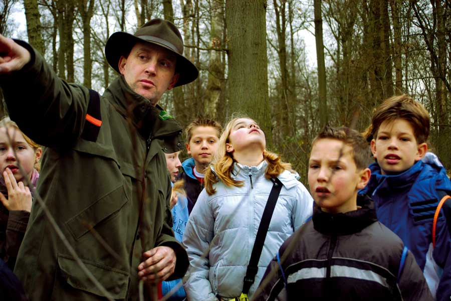 Een boswachter wijst iets in het bos aan aan een groep kinderen