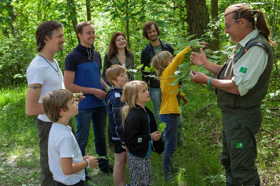 Een boswachter leert een groep kinderen en hun ouders in het bos over de natuur