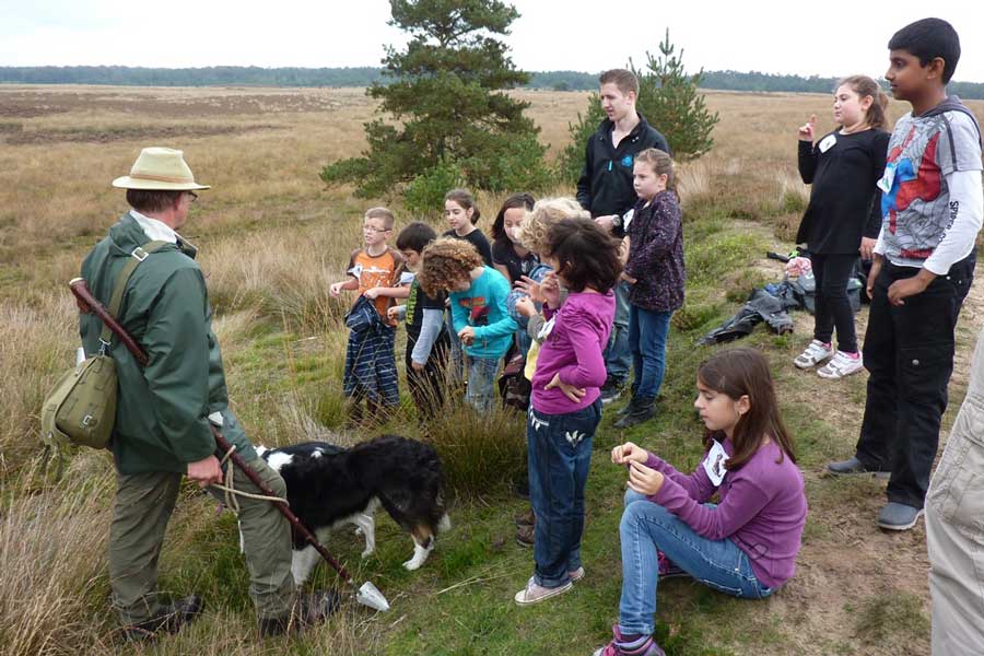 Een groep kinderen luistert naar de herder in een heidegebied