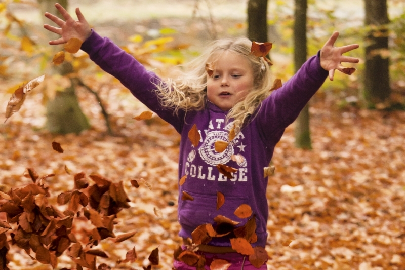 meisje speelt met herfstblaadjes