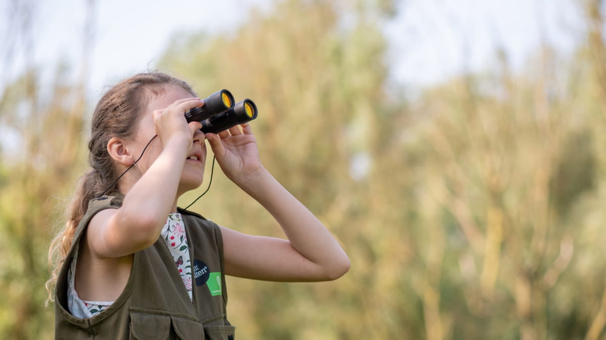 Twee kinderen staan met hun verrekijker in een natuurgebied