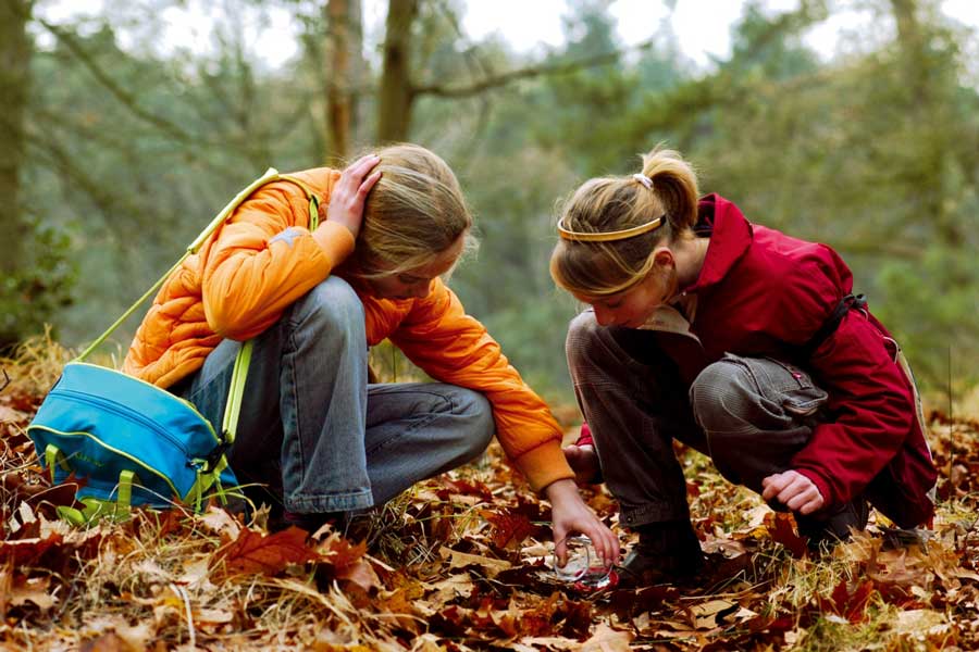 Twee meisjes zoeken tussen de gevallen bladeren in het bos