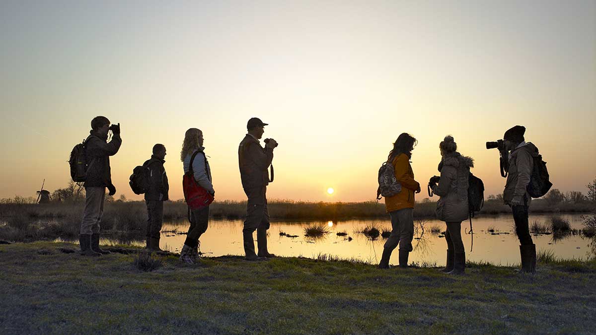 Een groep staat met de boswachter aan de rand van een meer te kijken naar de zonsopgang