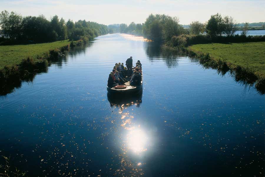 Een groep mensen maakt een boottocht met een boswachter over een ringvaart