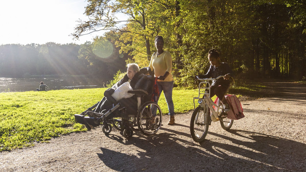 Vrouw wandelt met dame in rolstoel en kind in park
